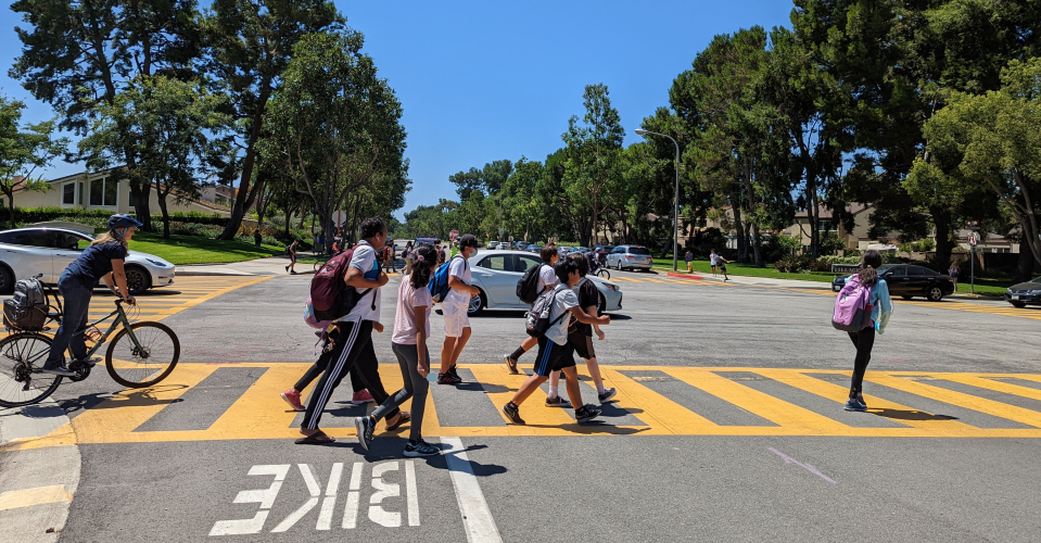 Kids with backpacks walking and riding bikes in a crosswalk