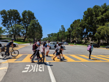 Kids with backpacks walking and riding bikes in a crosswalk